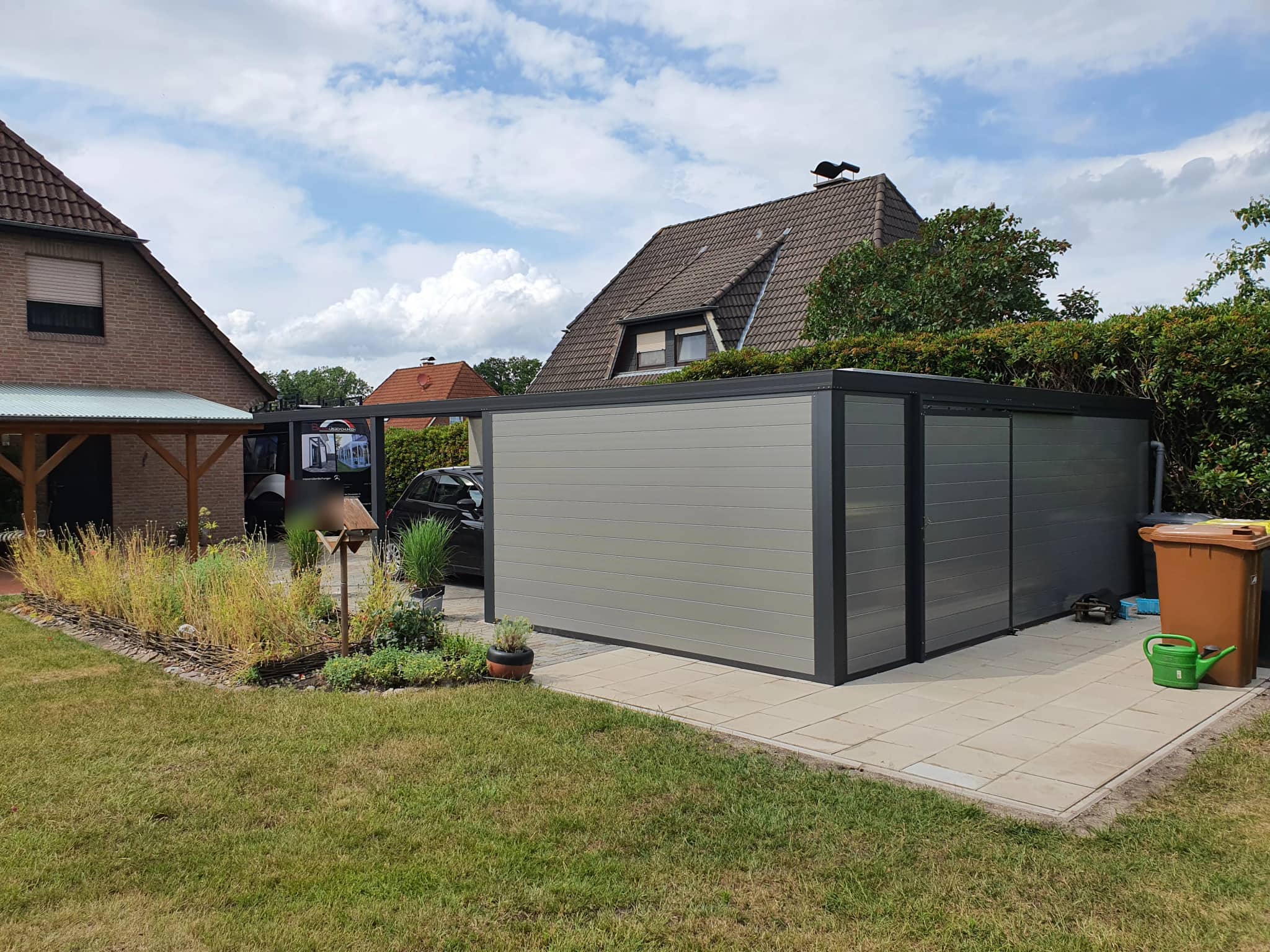 Flachdach-Carport aus Aluminium mit geschlossenen Paneelwänden neben einem Vorgarten