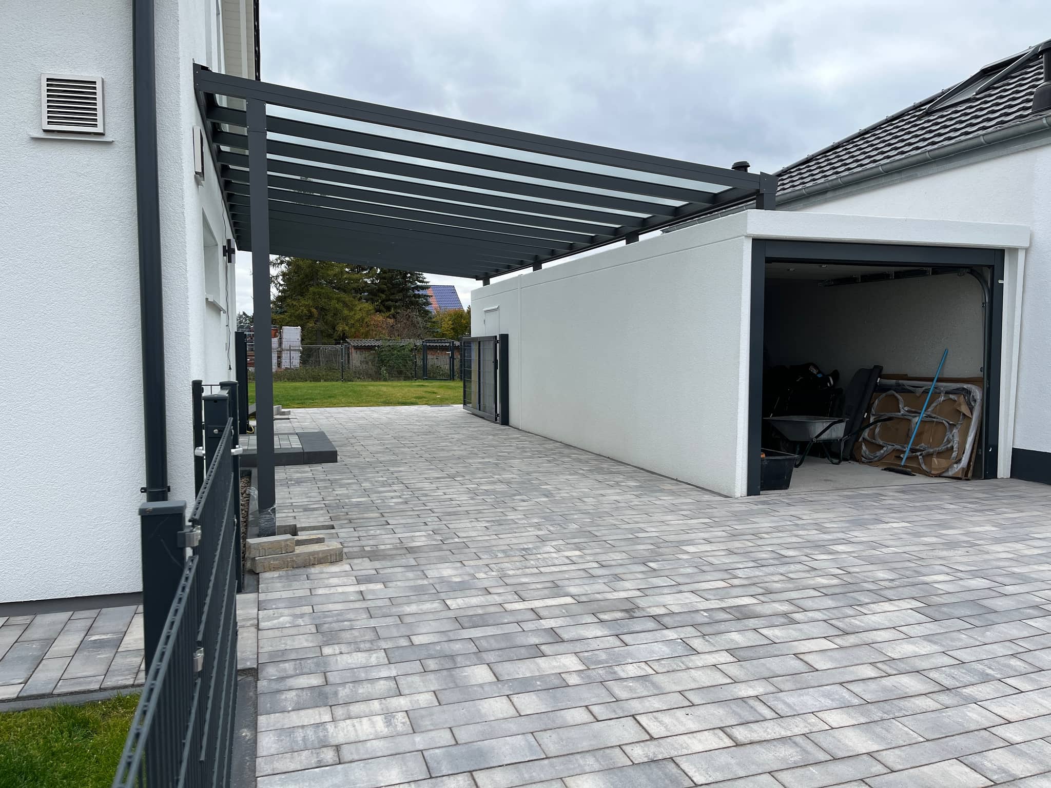 Carport aus Aluminium in Anthrazit mit lichtdurchlässiger Eindeckung zwischen Wohnhaus und Garage über gepflasterter Einfahrt