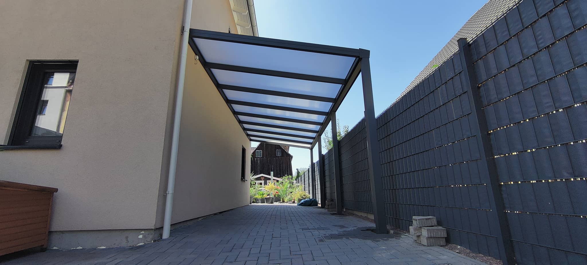 Carport aus Aluminium in Anthrazit mit lichtdurchlässiger Eindeckung an der Hauswand, seitlich eine blickdichte Sichtschutzwand