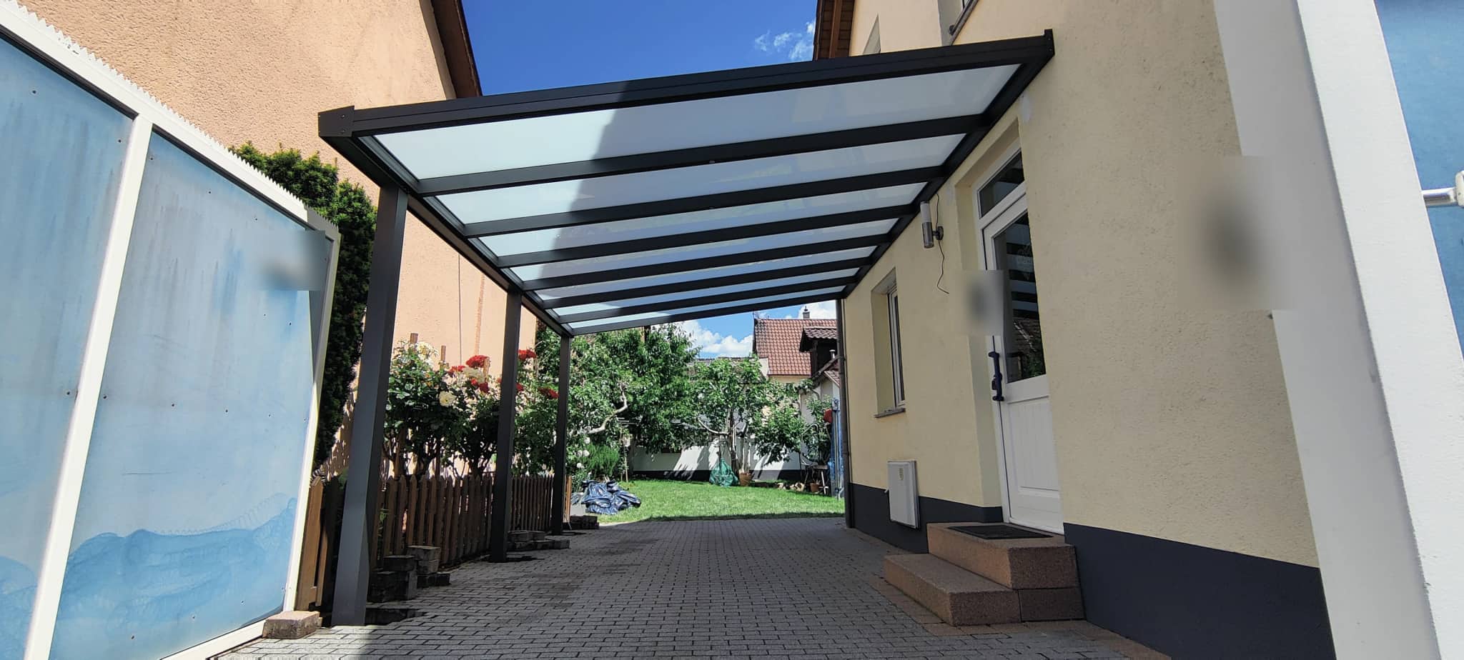 Carport aus Aluminium in Anthrazit mit lichtdurchlässiger Eindeckung über einer Hofeinfahrt zwischen Wohnhäusern