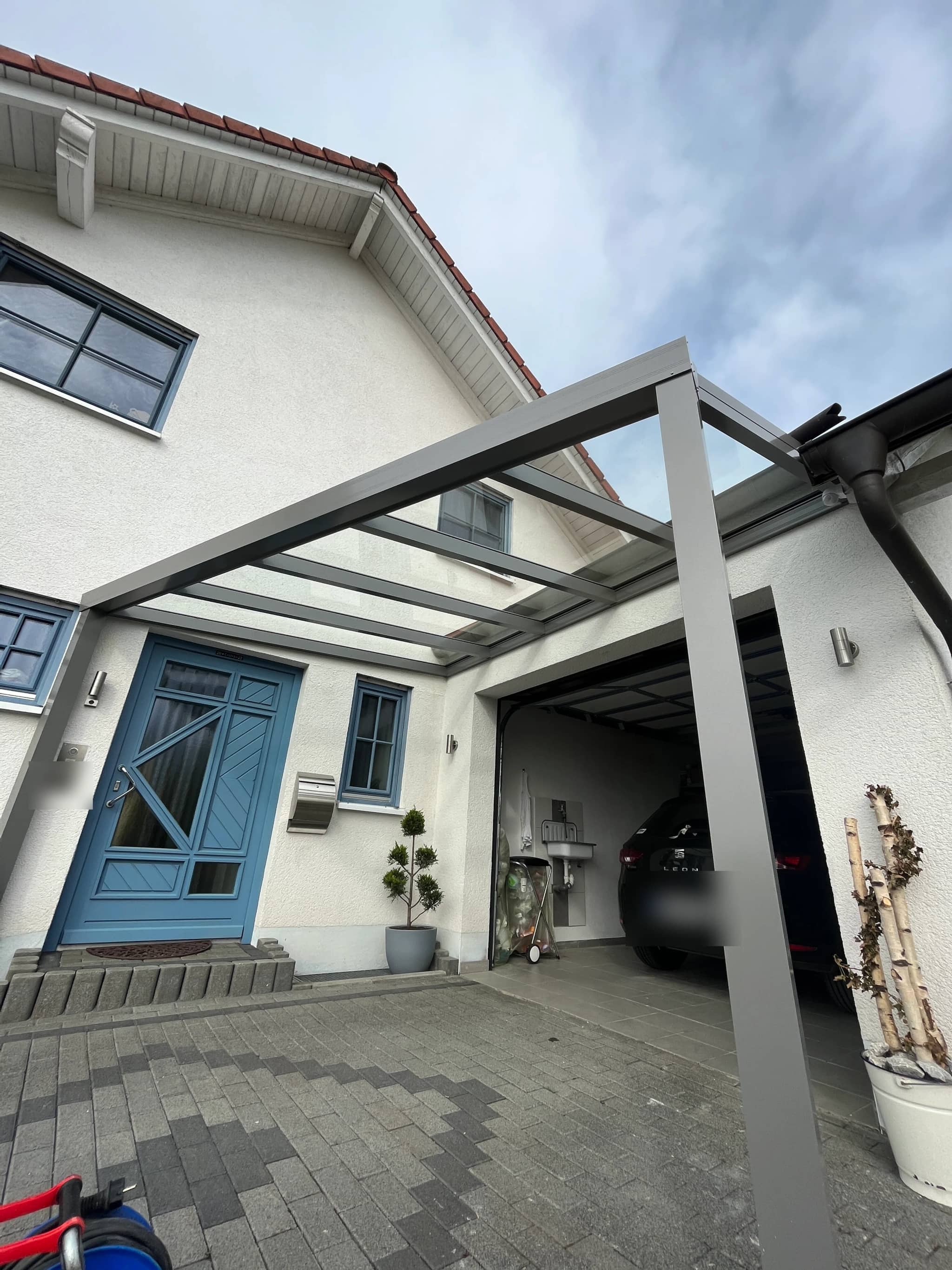 Carport bzw. Aluminium-Vordach mit lichtdurchlässiger Eindeckung über Eingang und Garagenzufahrt, anthrazitfarbene Konstruktion am Einfamilienhaus