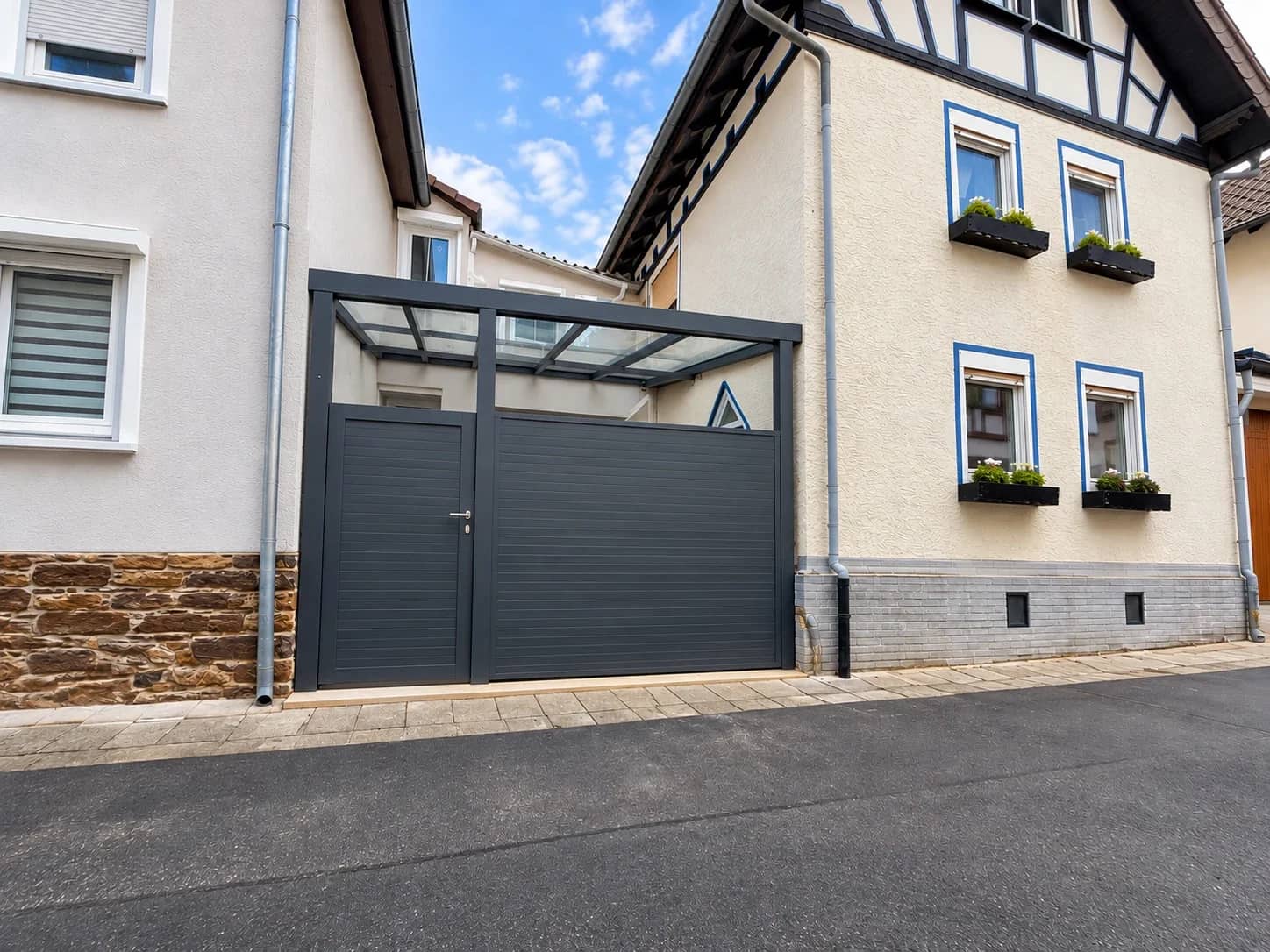 Carport-Zufahrt mit lichtdurchlässiger Überdachung und anthrazitfarbenem Tor zwischen zwei Wohnhäusern