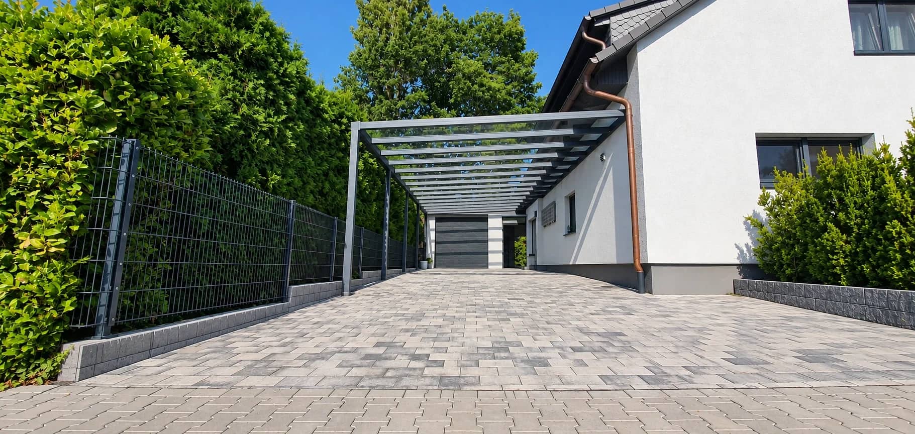 Carport in Aluminium mit lichtdurchlässiger Eindeckung über einer gepflasterten Einfahrt neben einem Wohnhaus