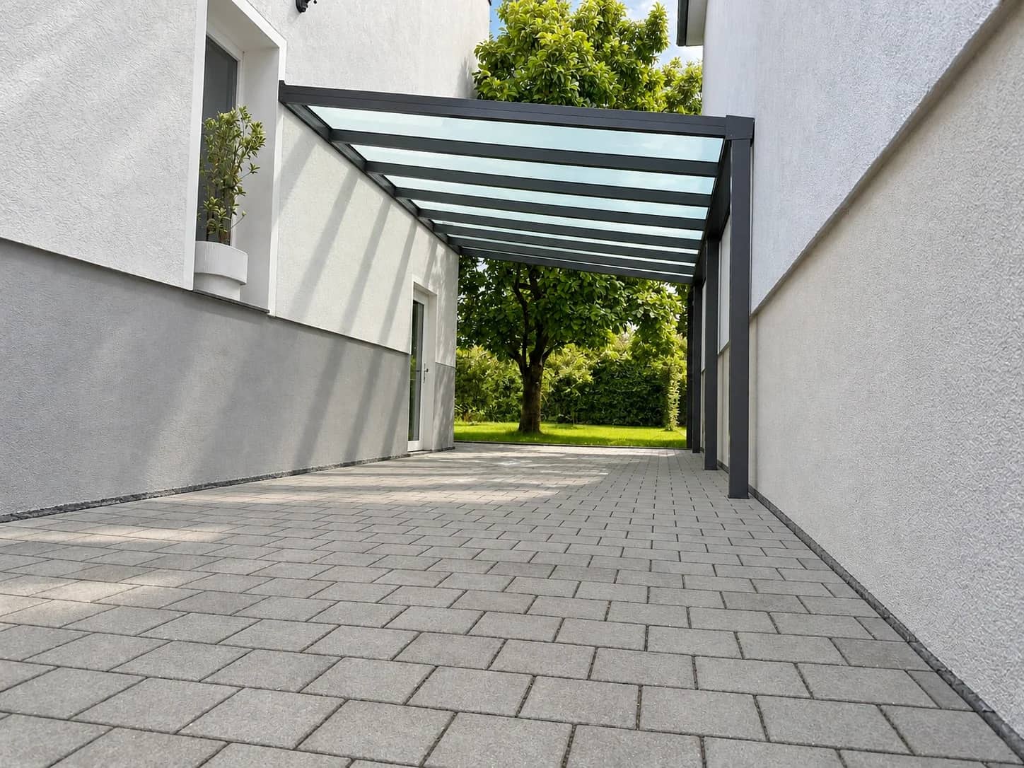 Carport mit anthrazitfarbenem Aluminiumrahmen und lichtdurchlässiger Eindeckung, offen an einer seitlichen Hofzufahrt zwischen zwei Hauswänden