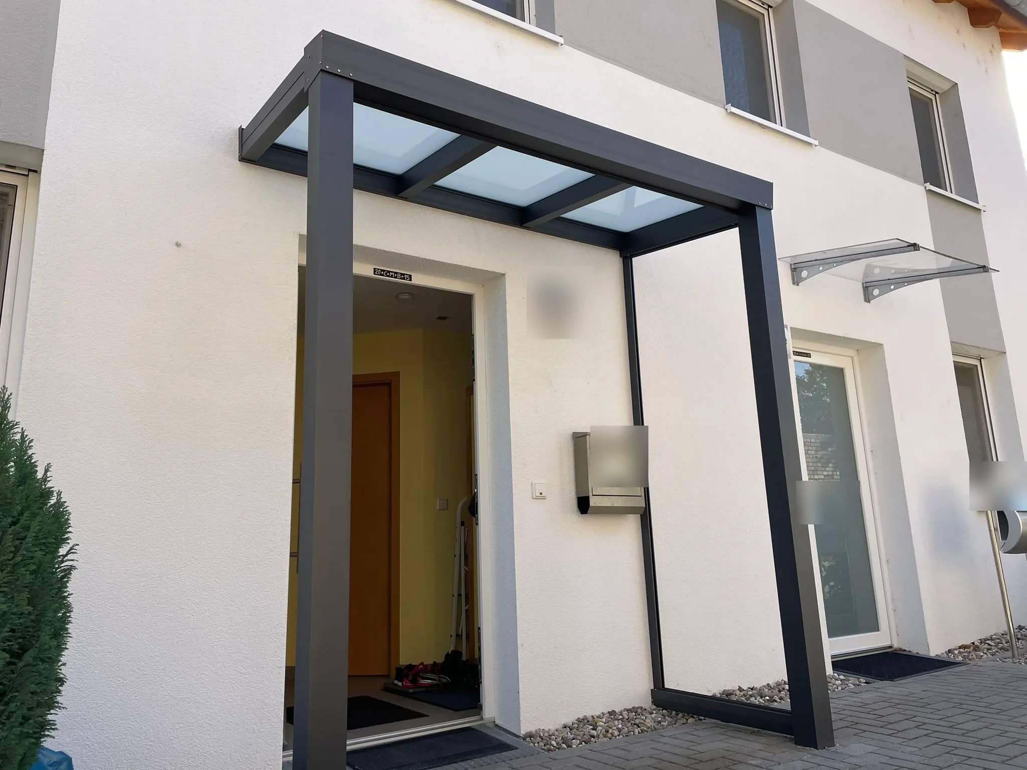 Eingangsüberdachung aus Aluminium in Anthrazit mit zwei Stützen und lichtdurchlässiger Eindeckung über der Haustür