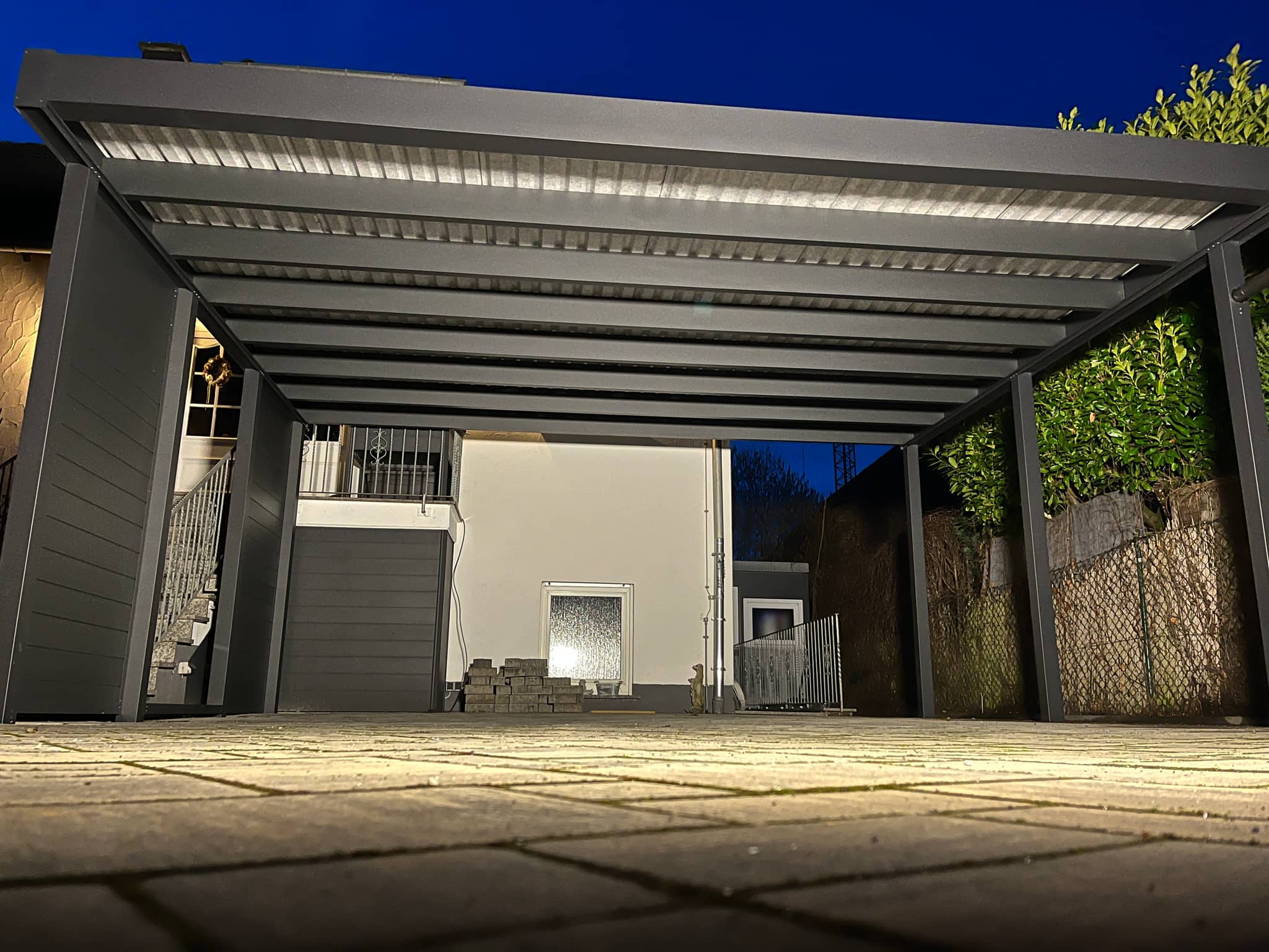 Flachdach-Carport aus Aluminium mit seitlichen Sichtschutzwänden und beleuchteter Dachfläche am Abend