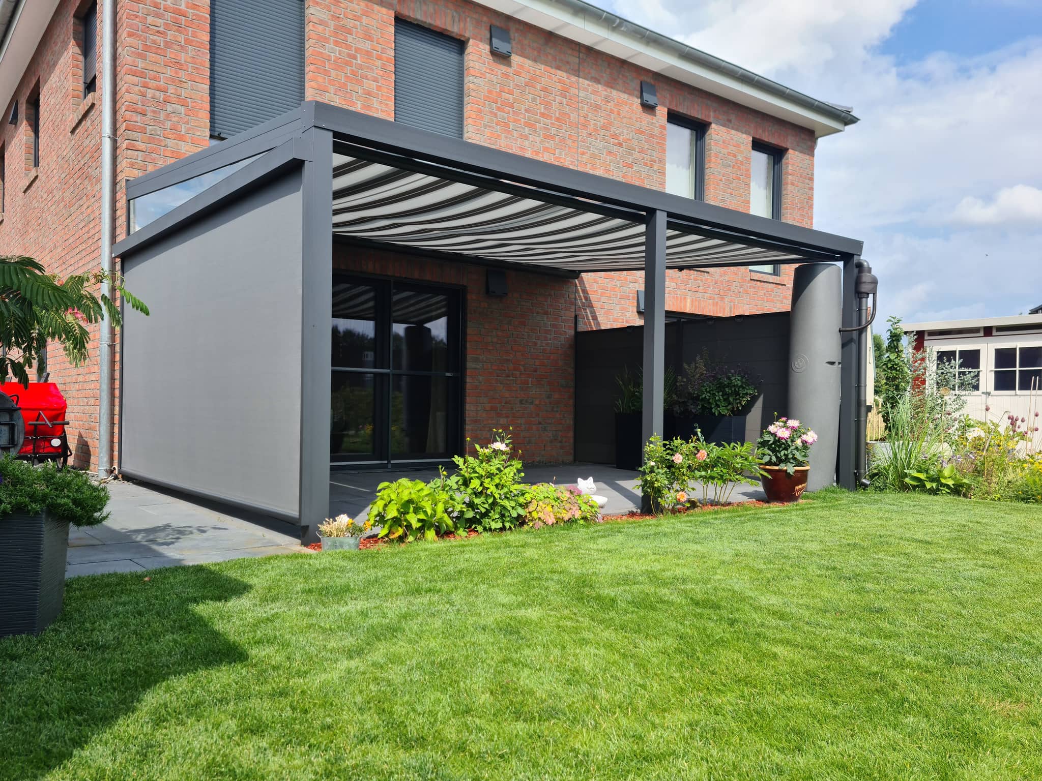 Terrassenüberdachung aus anthrazitfarbenem Aluminium mit Unterdach-Beschattung und seitlichem Sonnenschutz an einem Klinkerhaus
