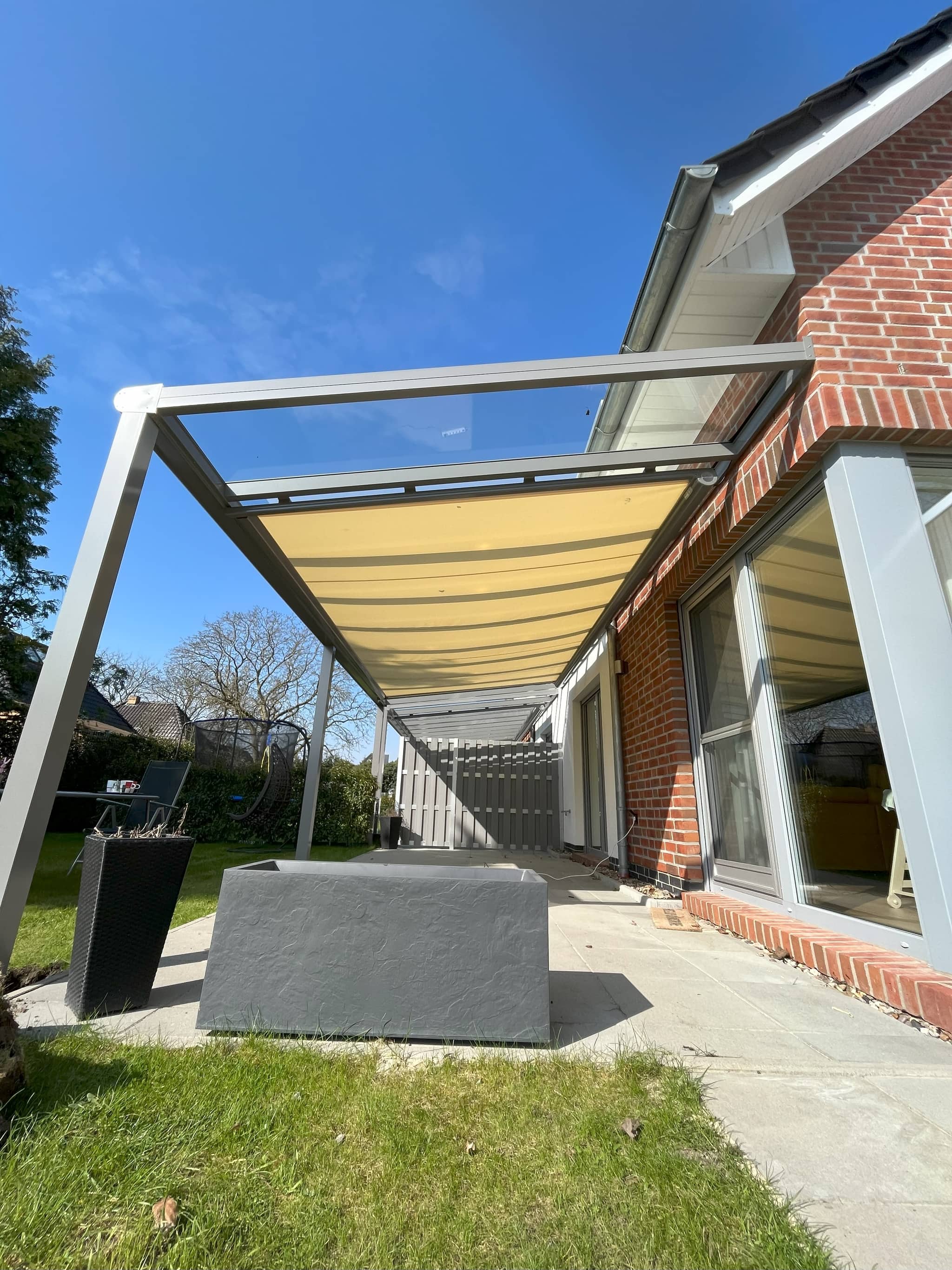 Markise als Beschattung unter einem Aluminium-Terrassendach mit hellem Tuch entlang der Hausfassade
