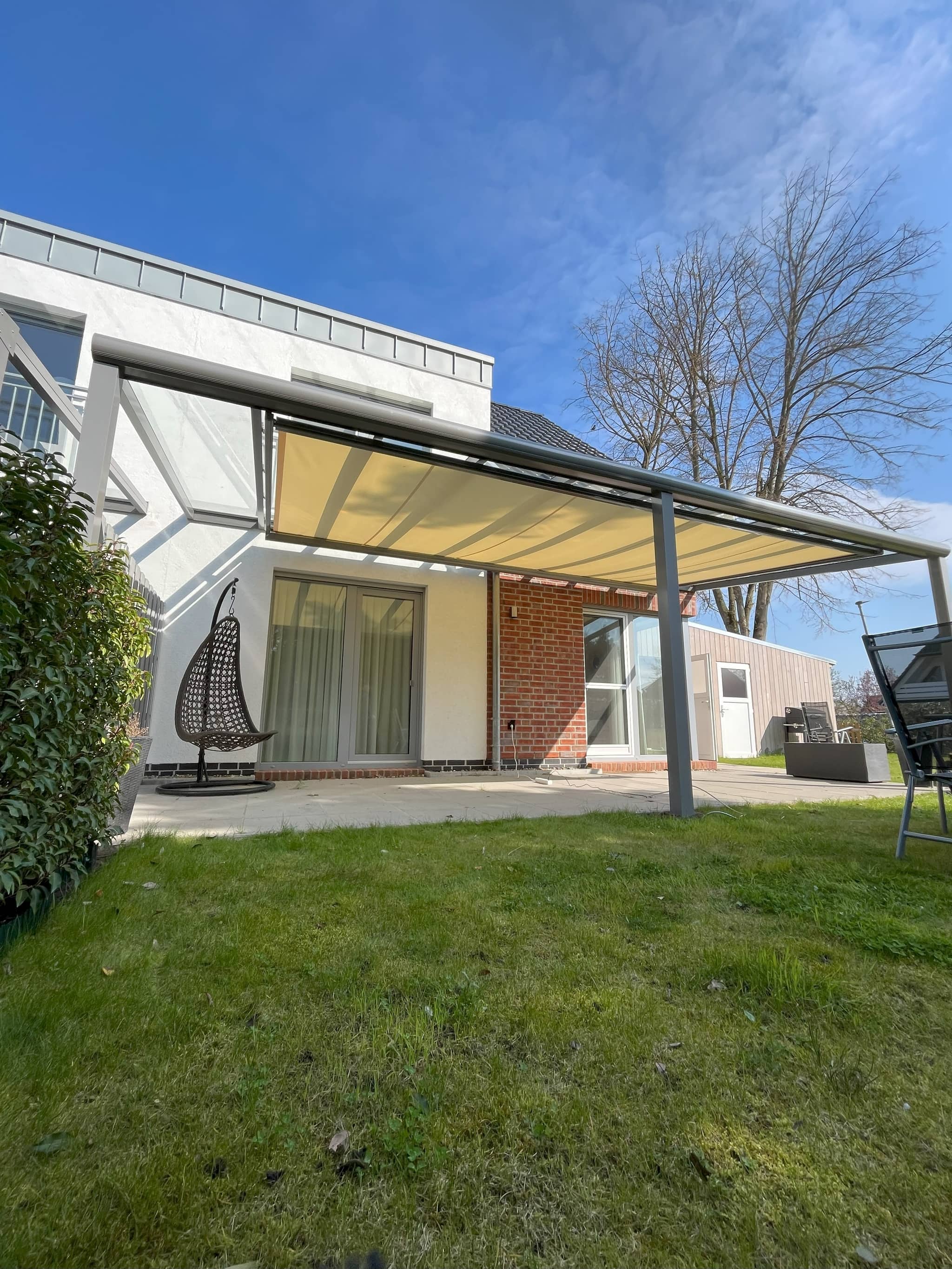 Unterdachmarkise mit hellem Tuch unter einem anthrazitfarbenen Terrassendach, davor Rasen