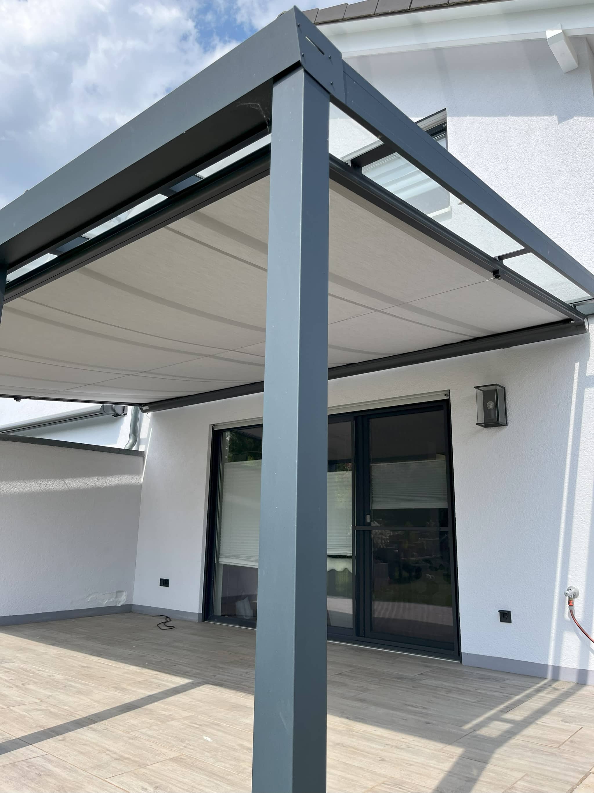 Markise als ausgefahrener Unterglas-Sonnenschutz unter einem anthrazitfarbenen Terrassendach am Wohnhaus