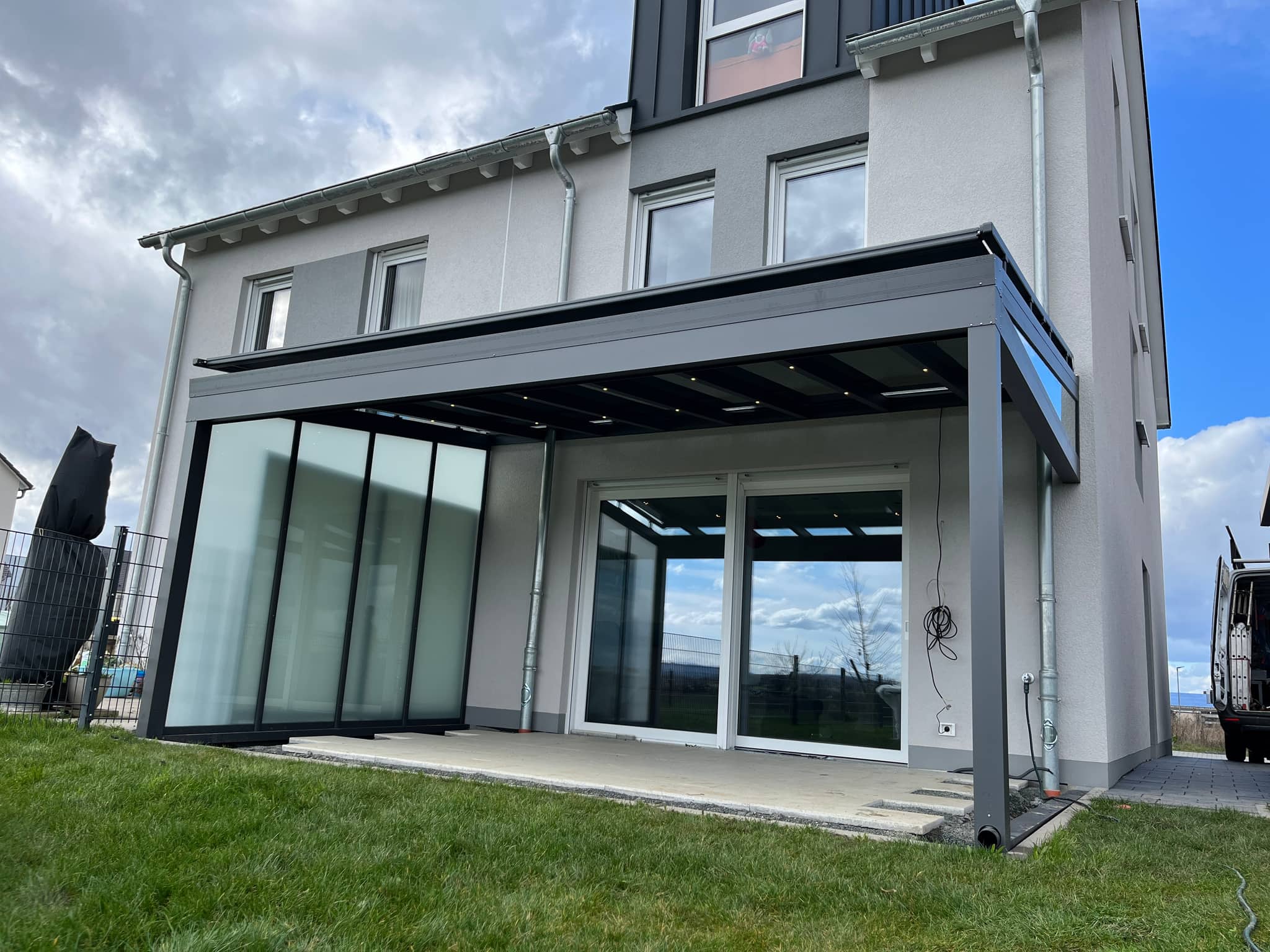 Aufdachmarkise auf einer Aluminium-Terrassenüberdachung mit seitlicher Verglasung am mehrgeschossigen Wohnhaus