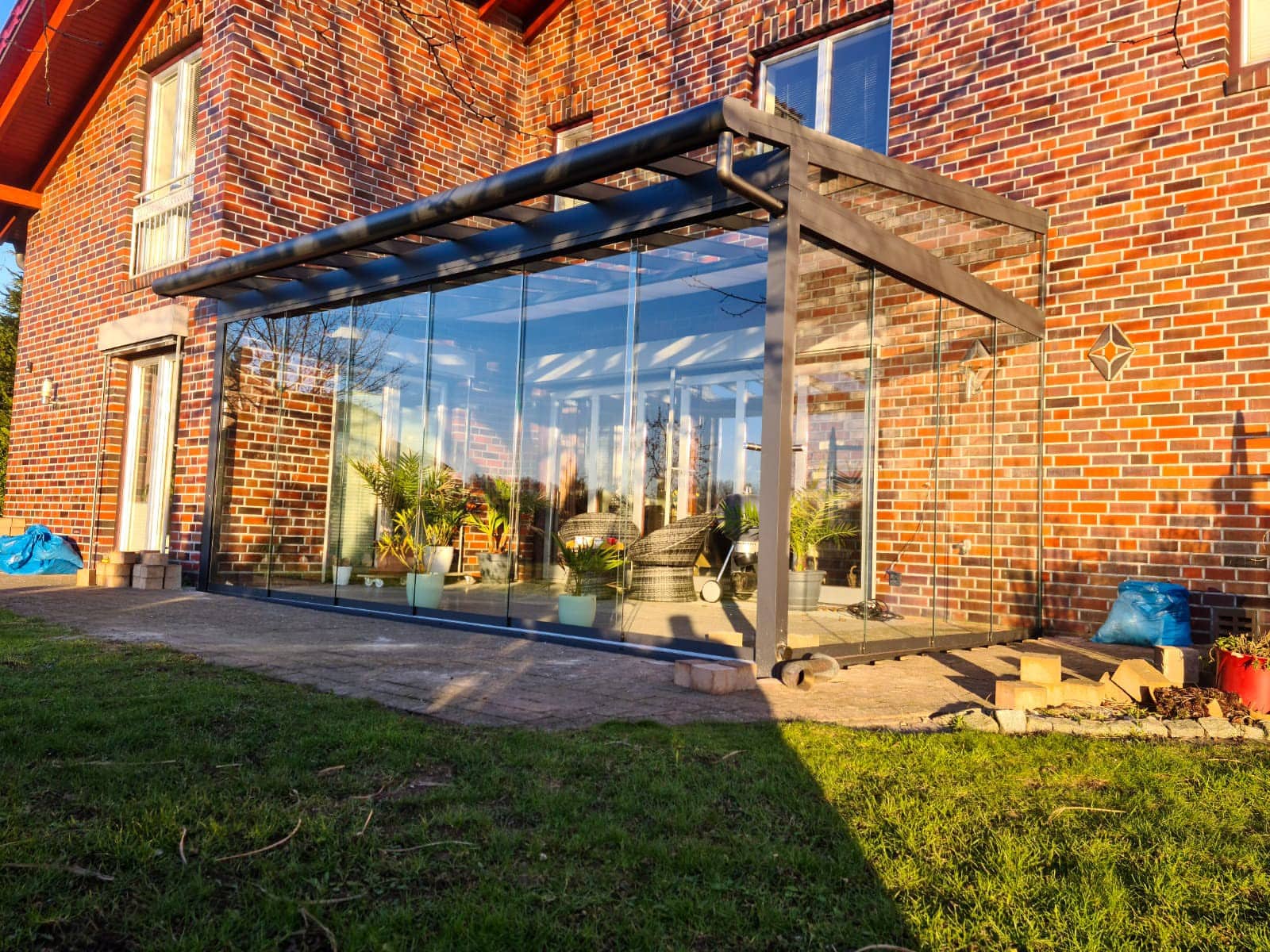 Sommergarten mit rahmenloser Ganzglas-Schiebefront und anthrazitfarbenem Aluminiumgestell an der Klinkerfassade