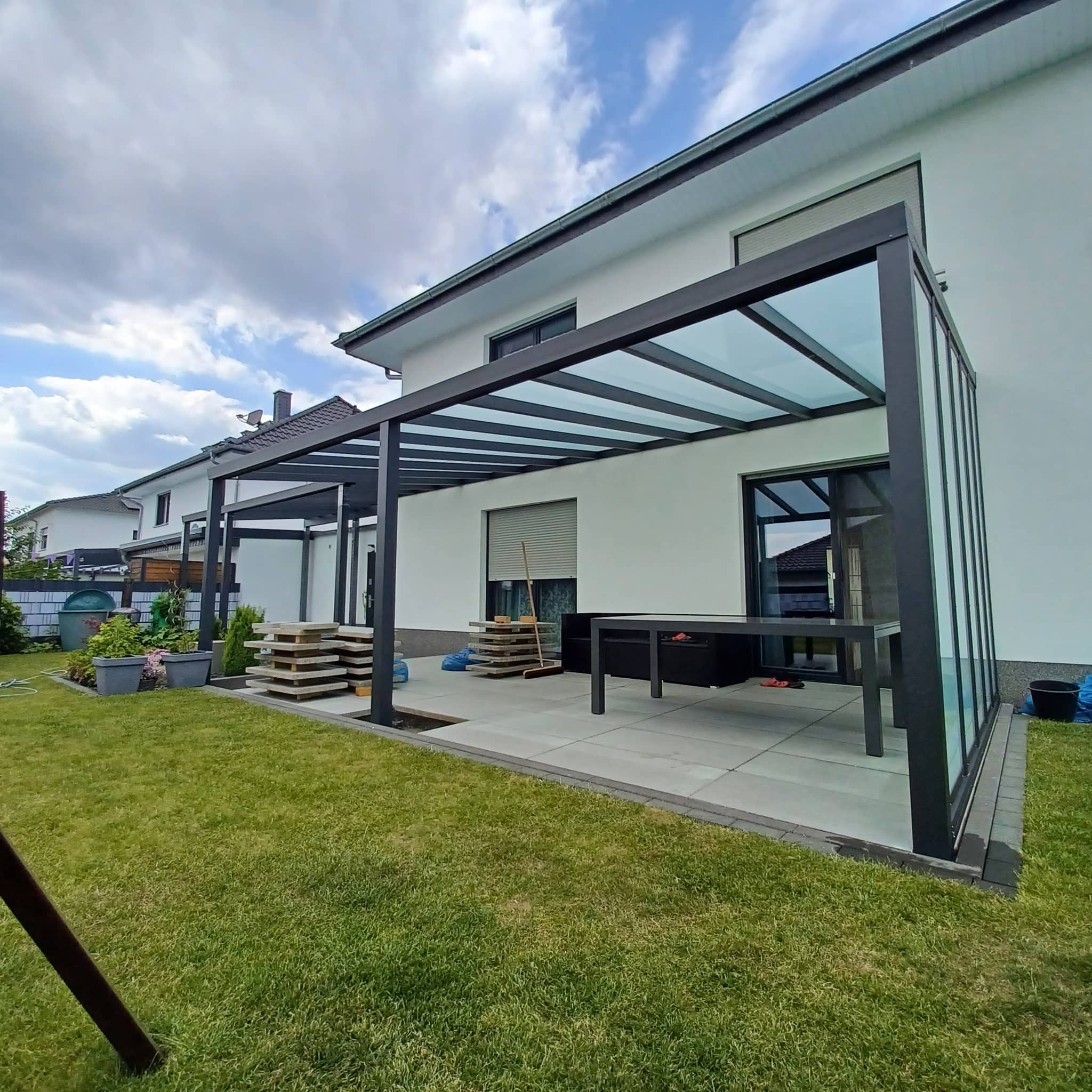 Terrassenüberdachung aus Aluminium in Anthrazit mit Glas-Seitenwand und lichtdurchlässigem Dach am Einfamilienhaus
