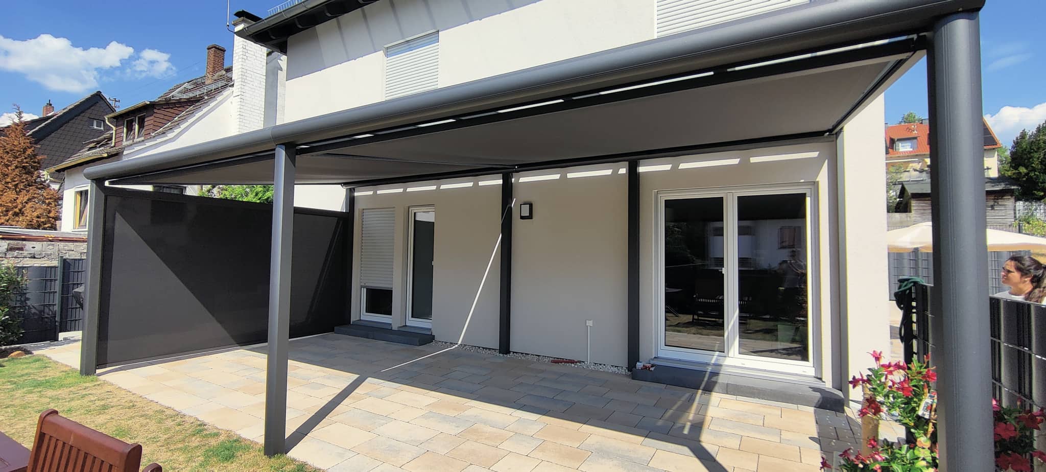 Langgezogene Terrassenüberdachung aus Aluminium in Anthrazit mit dunkler Panelwand an der Seite