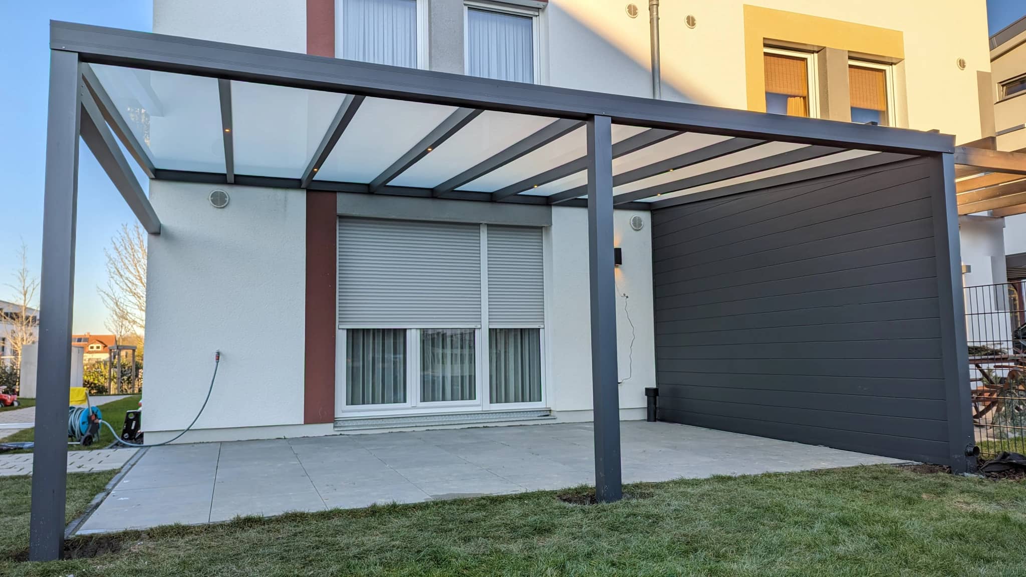 Terrassenüberdachung aus Aluminium in Anthrazit mit blickdichter Panel-Seitenwand an einem hellen Wohnhaus