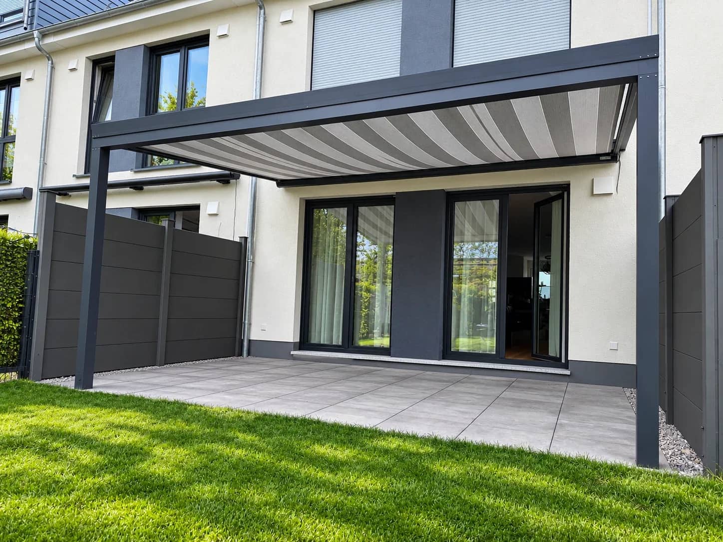 Terrassenüberdachung aus Aluminium in Anthrazit mit ausgefahrener Beschattung an der Hausfassade