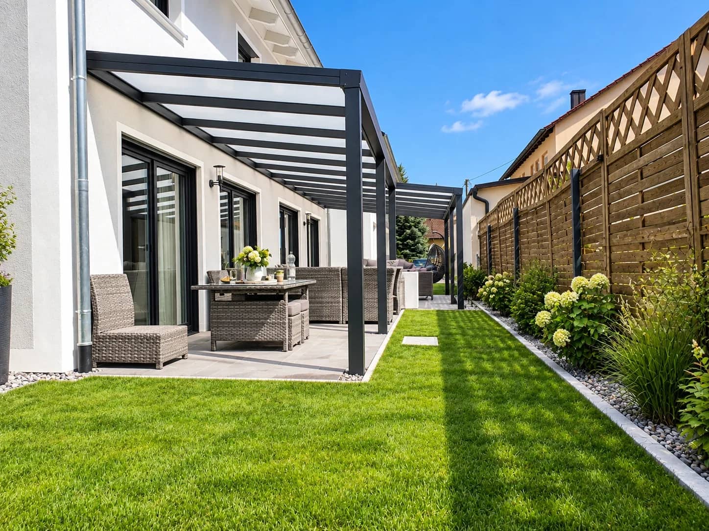 Terrassenüberdachung aus Aluminium in Anthrazit mit klarer Glaseindeckung, überdachte Sitzecke an der Hausfassade