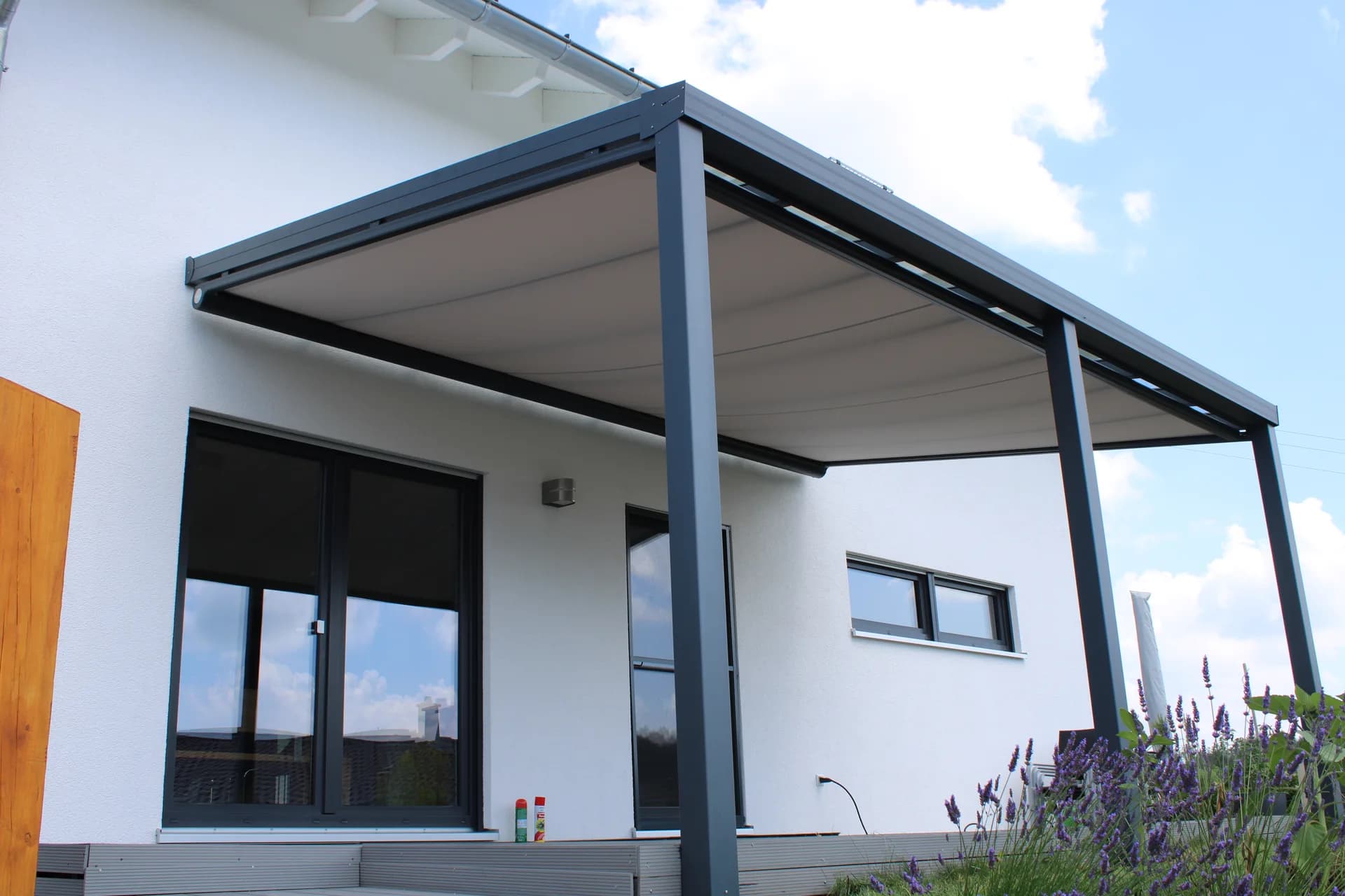 Anthrazitfarbene Aluminium-Terrassenüberdachung mit textiler Beschattung an einem hellen Wohnhaus