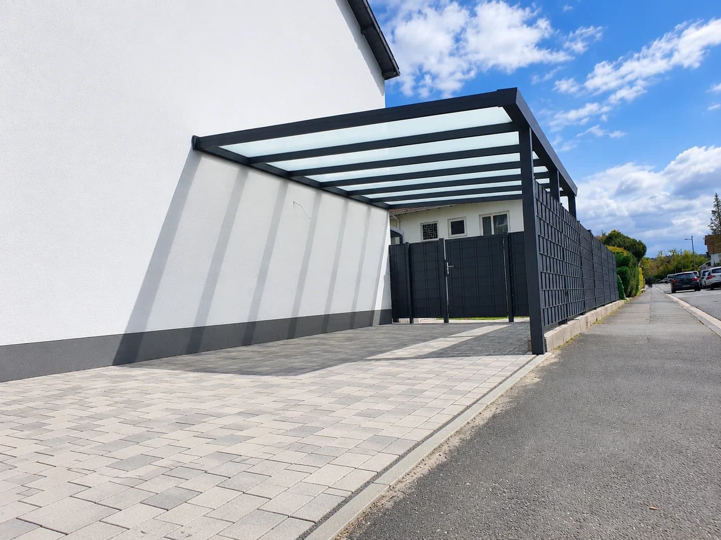 Anthrazitfarbener Aluminium-Carport mit Glasdach und seitlichem Sichtschutzelement an der Hauswand