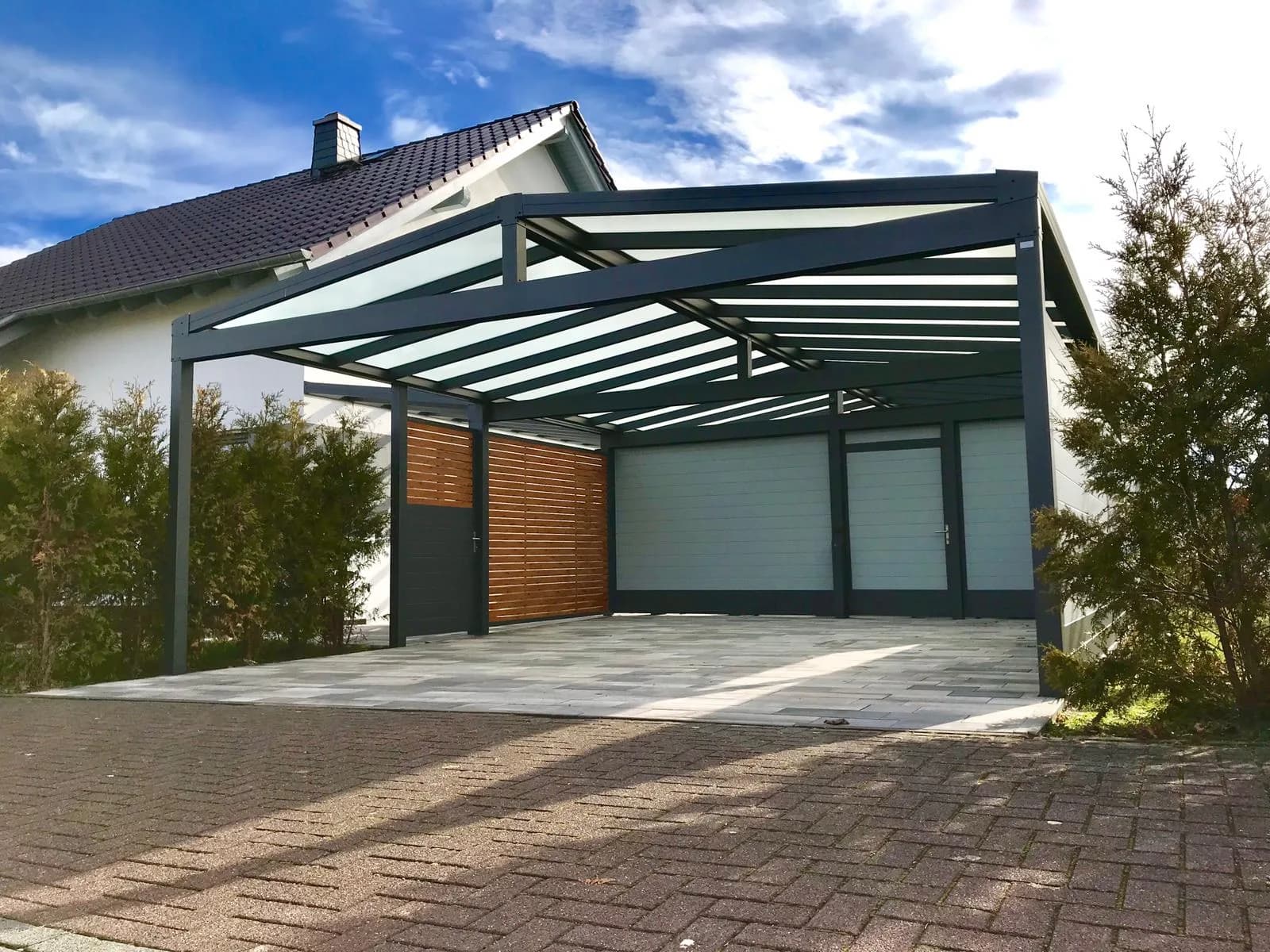 Carport aus Aluminium in Anthrazit mit lichtdurchlässiger Eindeckung vor einer Garage, seitlich ein Element in Holzoptik