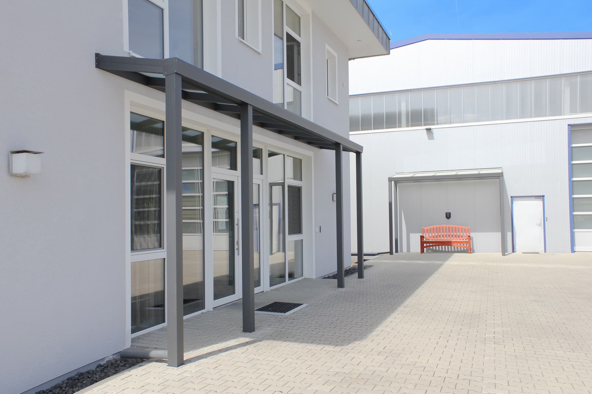 Eingangsüberdachung aus Aluminium in Anthrazit mit lichtdurchlässiger Eindeckung über dem Eingang eines Gewerbegebäudes