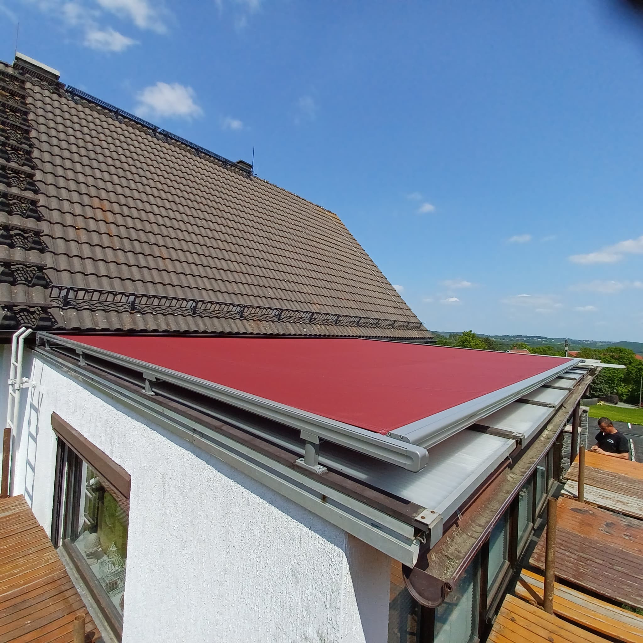 Markise mit rotem Tuch als Aufdach-Beschattung über einer verglasten Terrassenüberdachung – Referenzprojekt von Beckel Überdachungen