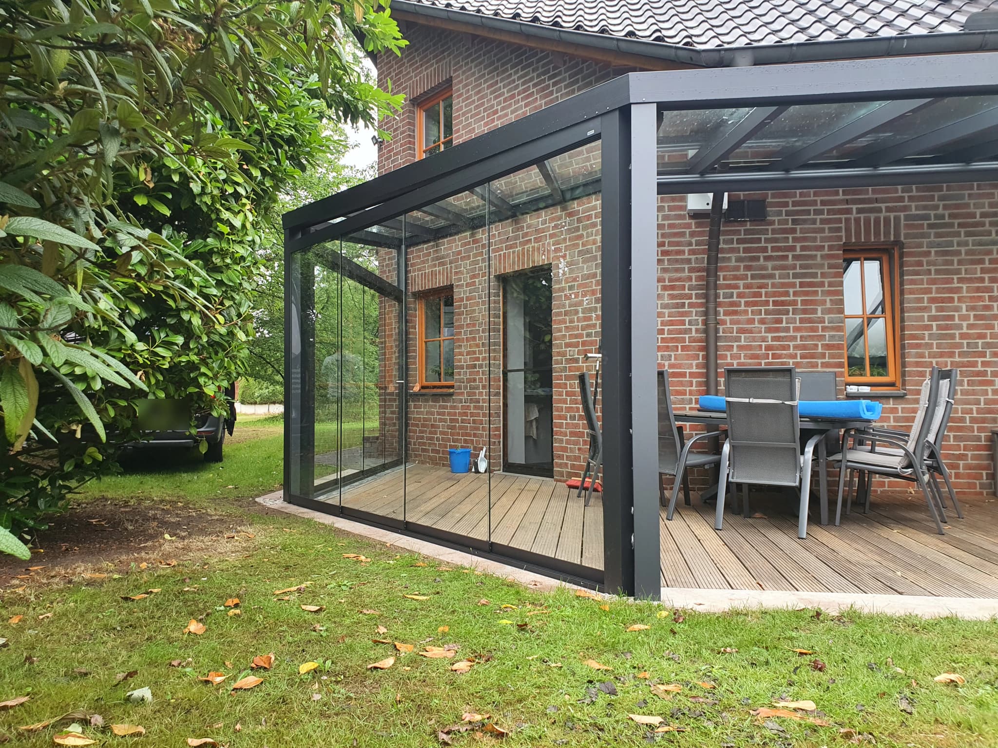 Sommergarten in Anthrazit mit umlaufenden Glasschiebeelementen, als Anbau an ein Backsteinhaus mit Terrassenmöblierung