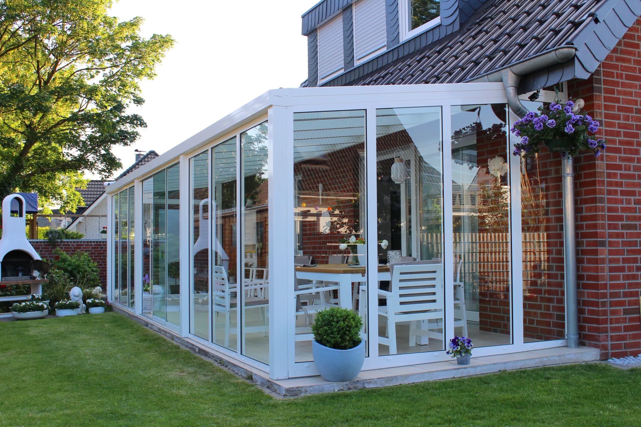 Sommergarten aus weißem Aluminium mit raumhohen Glaswänden am Klinkerhaus, davor Rasen
