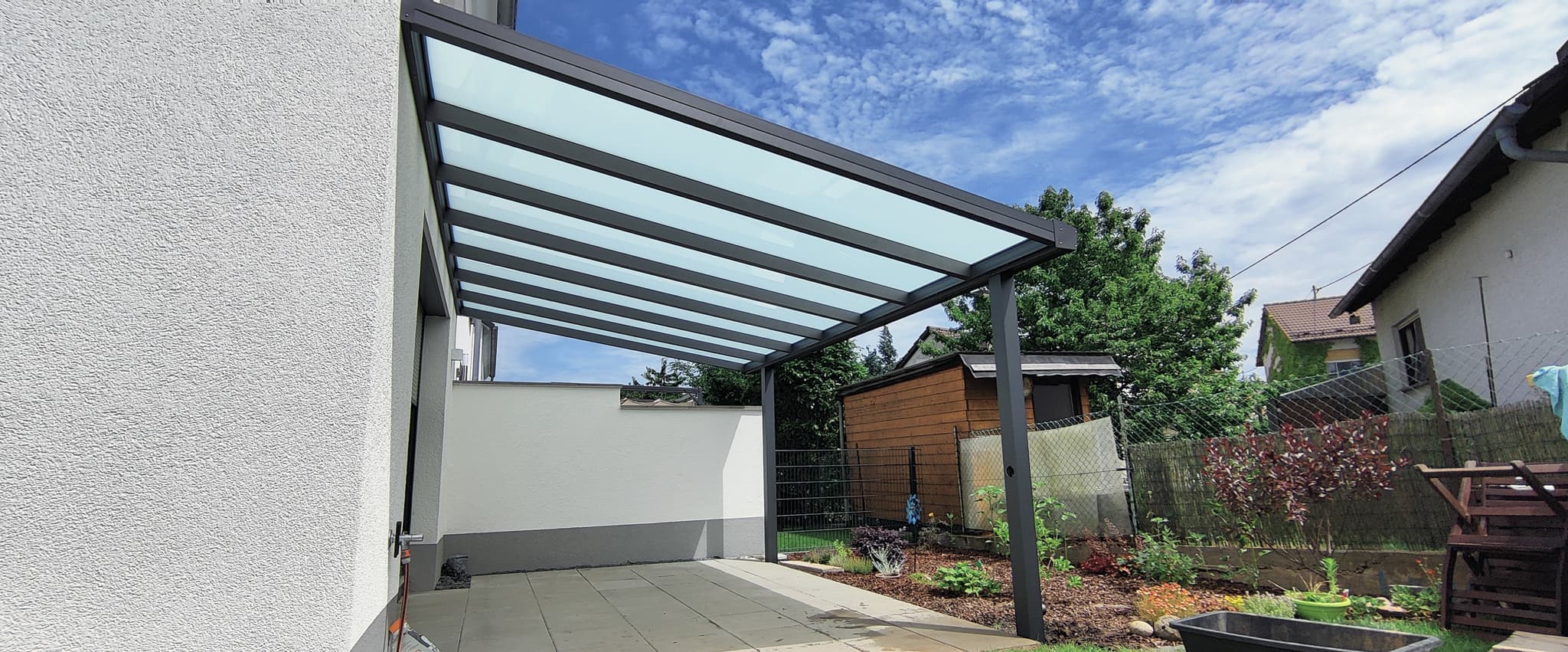 Terrassenüberdachung aus Aluminium in Anthrazit mit lichtdurchlässiger Eindeckung, an die Hauswand angebaut mit schlanken Sparren