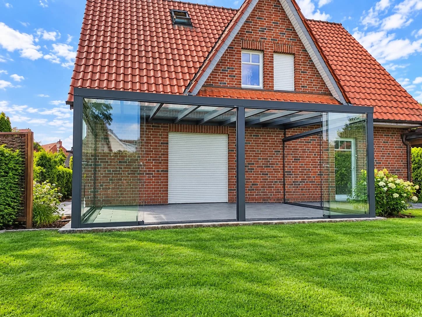Terrassenüberdachung in Anthrazit mit lichtdurchlässiger Eindeckung und gläsernen Seitenwänden vor einem Backsteinhaus