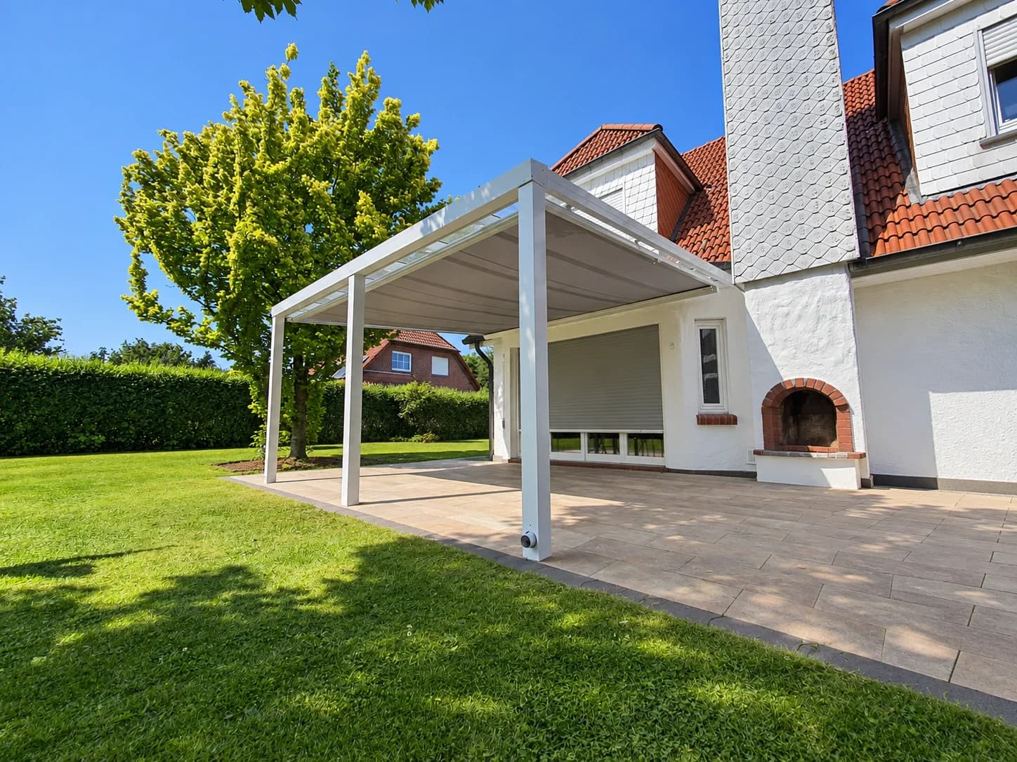 Markise unter einer weißen Terrassenüberdachung aus Aluminium mit hellem Tuch über einer Terrasse am Einfamilienhaus